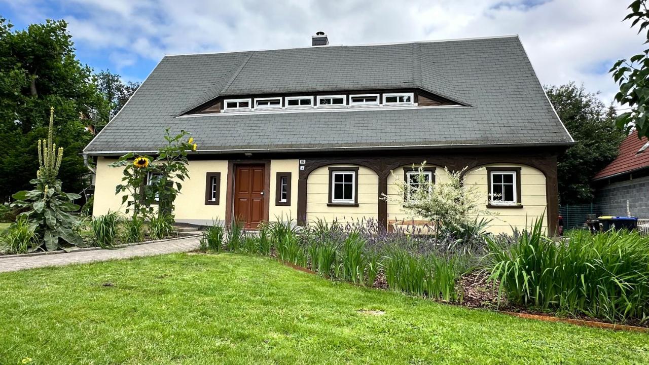 Ferienhaus Rudi von vorn: das lange Haus mit steilem Dach und Gaubenband, davor Rasen und ein blühendes Staudenbeet