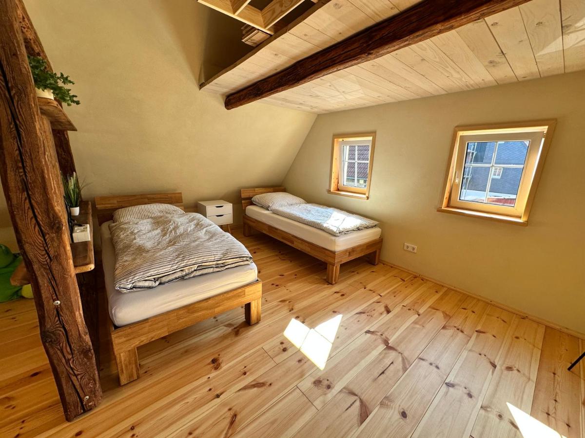 Schlafzimmer mit zwei Einzelbetten, einem alten Holzbalken an der Wand und zwei Fenstern