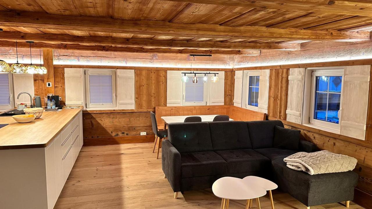 Offener Wohnraum mit Kücheninsel, Sofa und Essplatz unter einer Holzbalkendecke